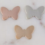Three metal butterfly-shaped charms on marble