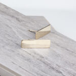 Gold rectangular bar stud earrings on wood