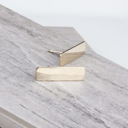 Gold rectangular bar stud earrings on wood