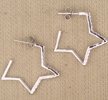 Silver star-shaped hoop earrings on beige fabric