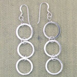 Silver triple hoop dangle earrings on beige fabric